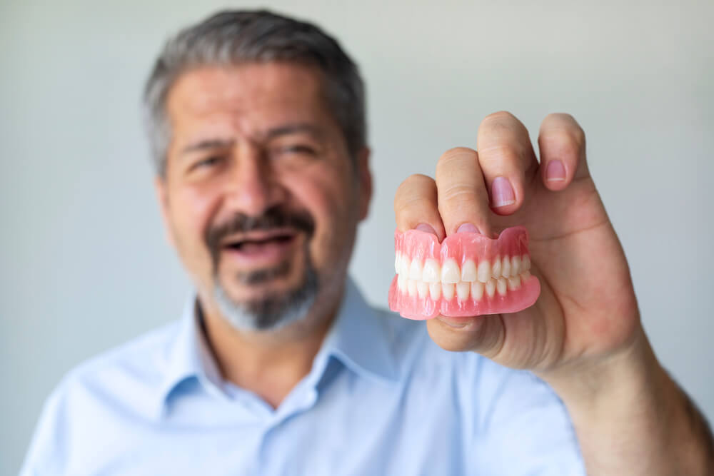 An old gray-haired man holds his denture.