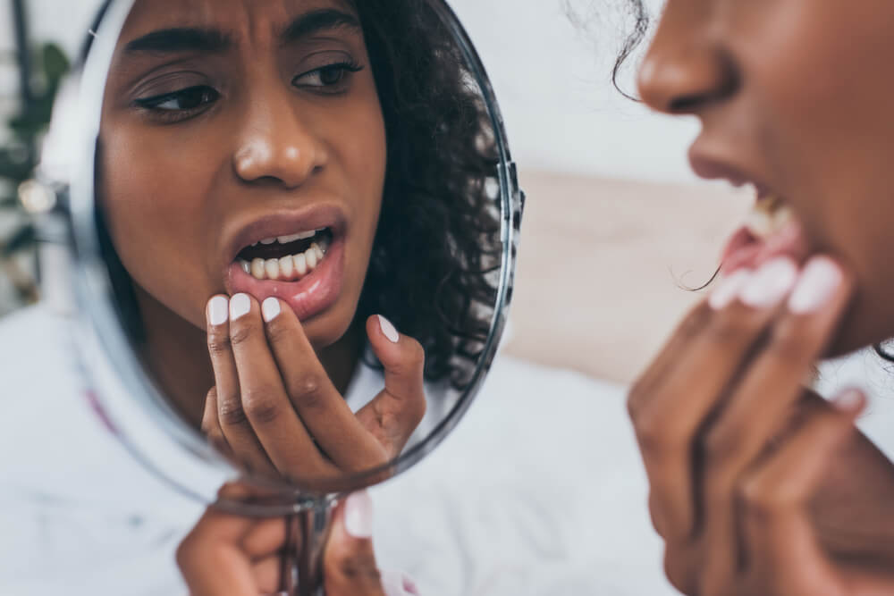 young woman looking at mirror while suffering from tooth pain