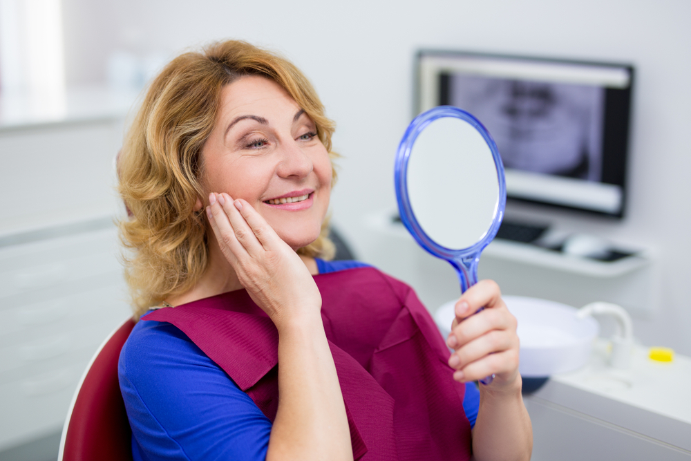 Woman smiling in the mirror after getting Dentures