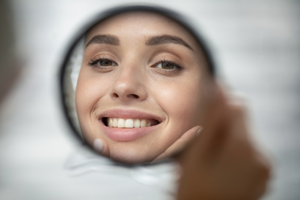 Woman smiling in the mirror after receiving Smile Transitions