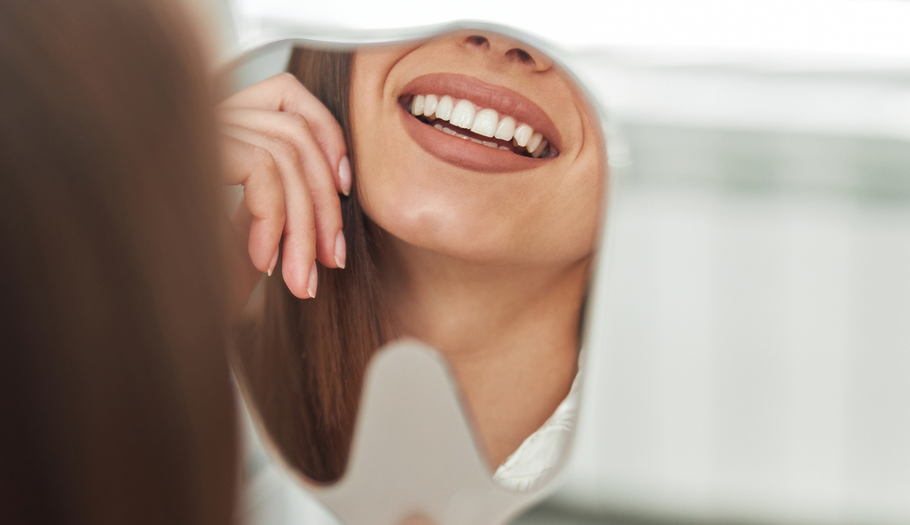 Woman smiling in the mirror after receiving Cosmetic Dentistry